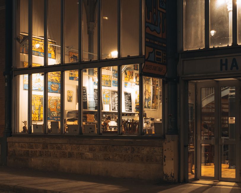 Warm glow from a cozy urban cafe with large glass windows at night.