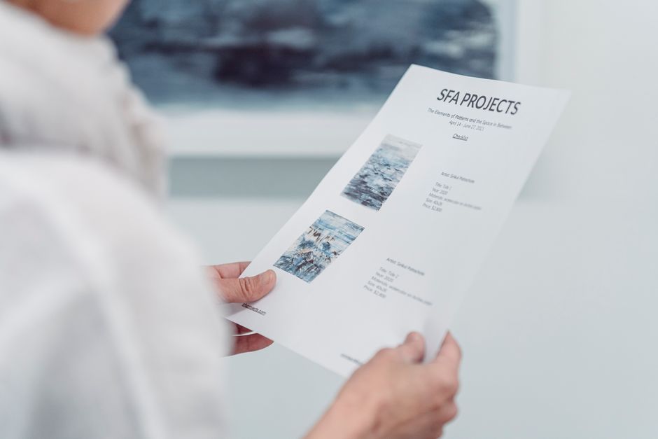 A person holds and reviews an SFA Projects document inside an art gallery.